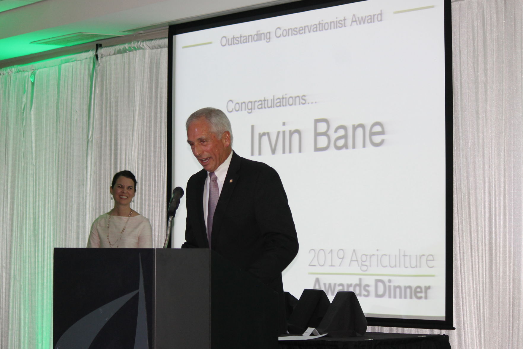 Farmer Irvin Bane of Bellflower accepts the award for Outstanding Conservationist as Master of ceremonies, Carrie Muehling , smiles at his acceptance speech